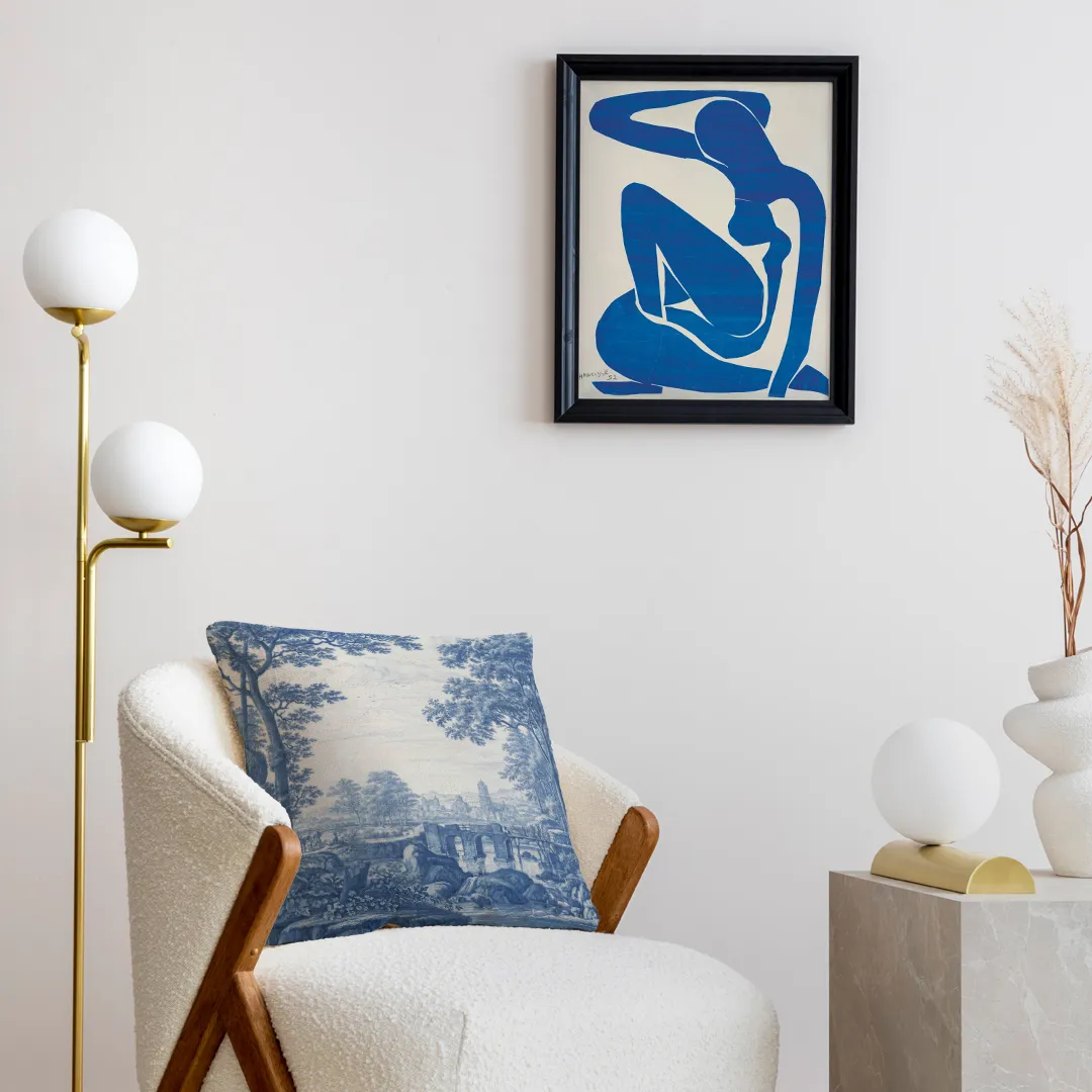 Poduszki dekoracyjne leżące na białym fotelu w jasnym, nowoczesnym wnętrzu. Na ścianie obraz ukazujący pracę Henriego Matisse'a.